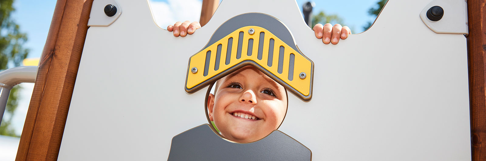 A young boy looks through a cut out panel on a playground unit which is themed like a knight. 